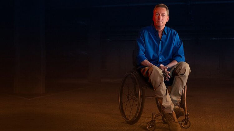 Frank Gardner in a wheelchair in a darkly lit building
